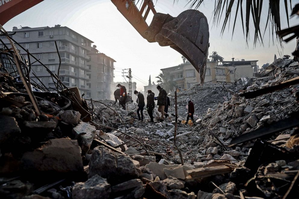 PHOTO: Workers stand on top of a collapsed building as a digger works its way through the debris, Feb. 13, 2023 in Hatay, Turkey.