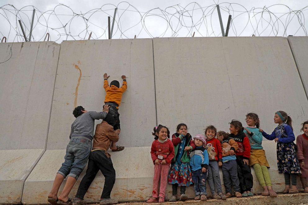 PHOTO: Displaced Syrian children try to climb over the Turkish border wall at an informal camp in Kafr Lusin village in Idlib, Syria, Feb. 21, 2020.