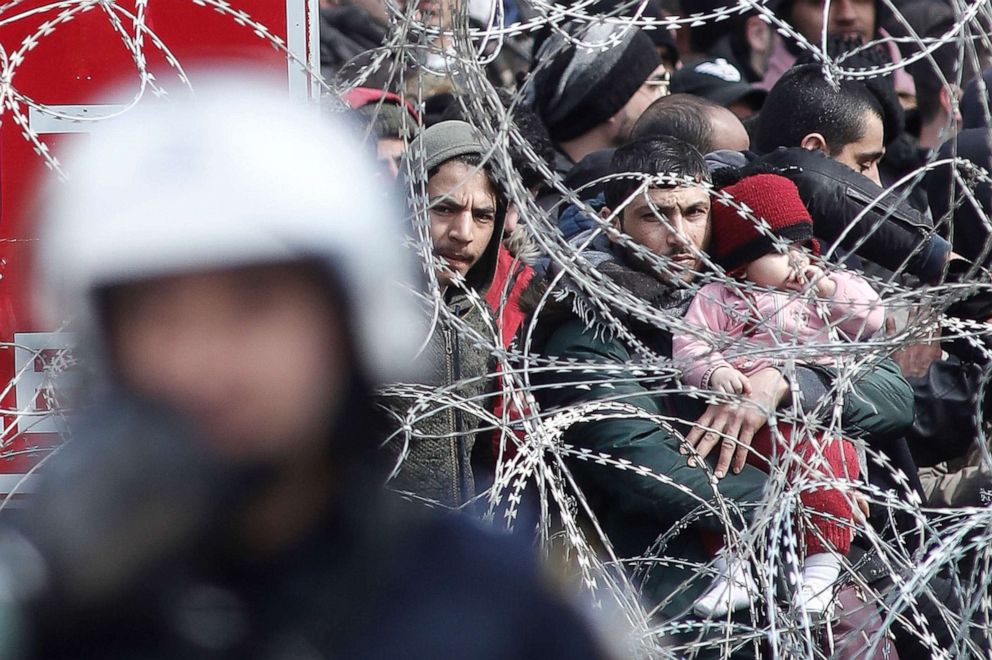 PHOTO: A man holding a child looks through barbed wire as migrants and refugees gather on the Turkish side of the closed Kastanies border crossing between Greece and Turkey, near the Evros River, in an attempt to cross into Greece, March 2, 2020.