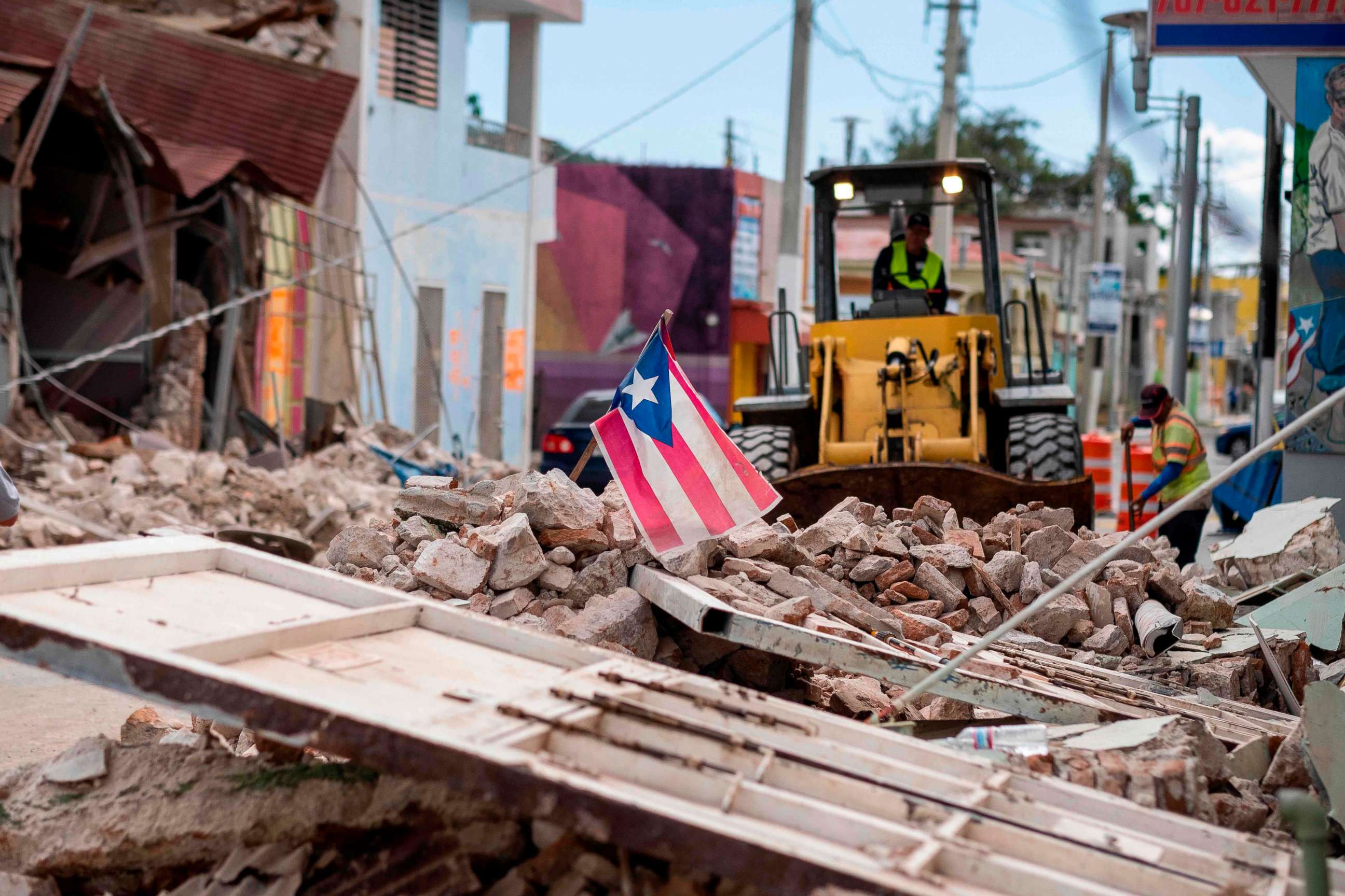 PHOTO: A Puerto Rican flag waves on top of a pile of rubble as debris is removed from a main road in Guanica, Puerto Rico, Jan. 8, 2020, one day after the earthquake. 