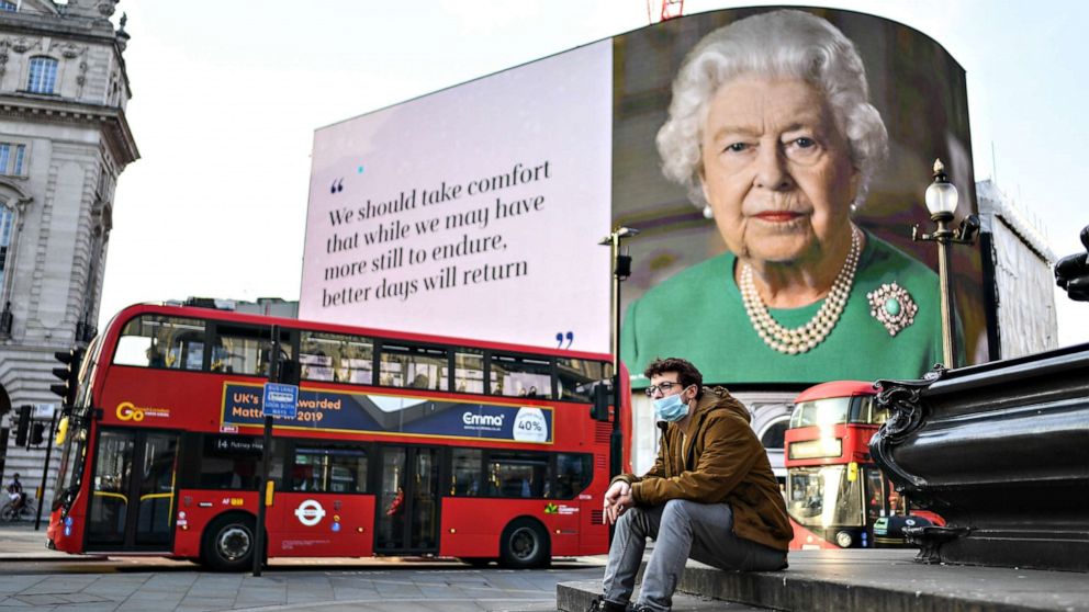 PHOTO: A man wearing a face mask sits in front of an image of Queen Elizabeth II with quotes from her broadcast to the nation on the coronavirus epidemic displayed on screens in Piccadilly Circus, on April 09, 2020, in London, England.