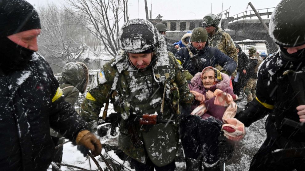 PHOTO: Ukrainian soldiers help an elderly woman to cross a destroyed bridge as she evacuates the city of Irpin, northwest of Kyiv, March 8, 2022.