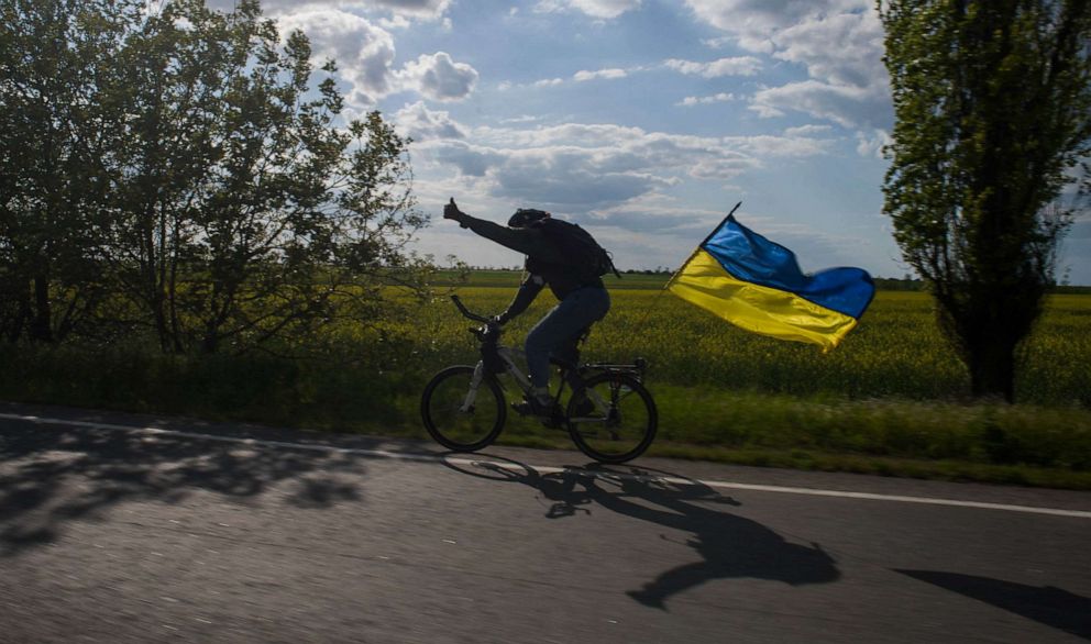 PHOTO: A cyclist brandishes a Ukraine flag in the disputed and reclaimed villages between Mykolaiv and Kherson, Ukraine, May 15, 2022.