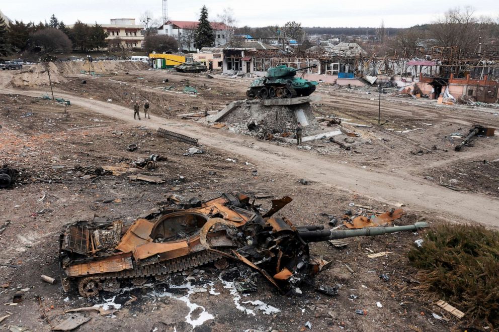 PHOTO: Local residents pass by a damaged Russian tank in the town of Trostyanets, east of capital Kyiv, Ukraine, on March 28, 2022. A monument to the Second World War is seen in background.