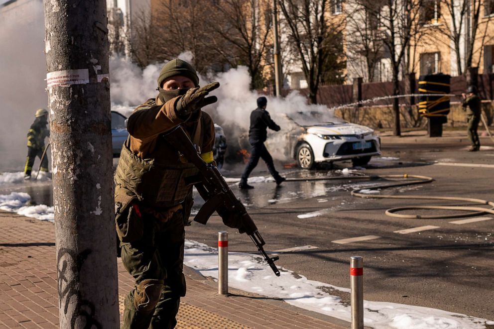 PHOTO: Ukrainian soldiers take positions outside a military facility as two cars burn in a street in Kyiv, Ukraine, Feb. 26, 2022.