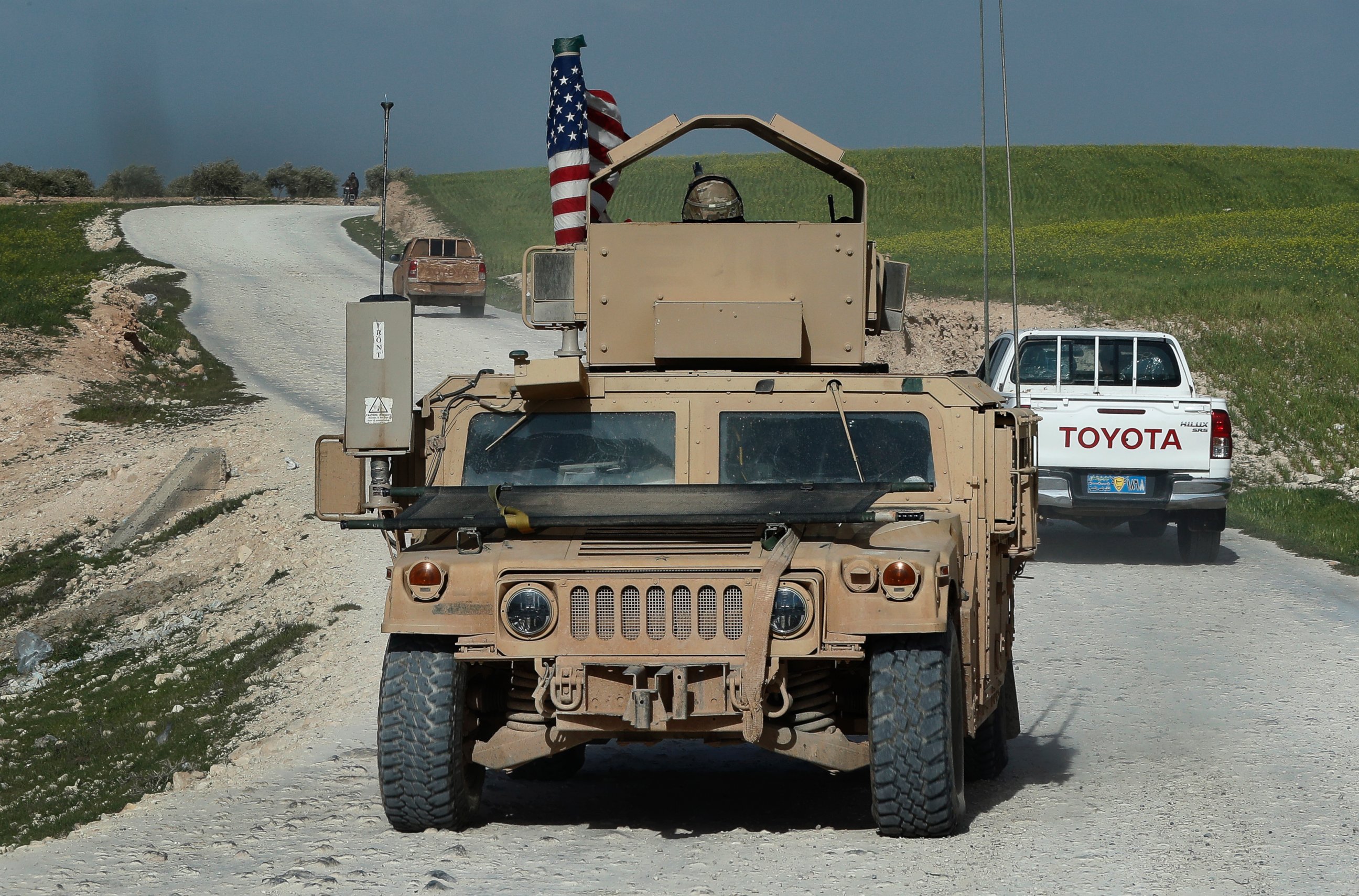 In this picture taken on Thursday, March 29, 2018, U.S. troop's humvee passes vehicles of fighters from the U.S-backed Syrian Manbij Military Council on a road leading to the tense front line with Turkish-backed fighters, north of Manbij town, Syria.