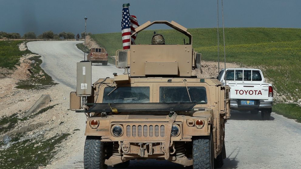 In this picture taken on Thursday, March 29, 2018, U.S. troop's humvee passes vehicles of fighters from the U.S-backed Syrian Manbij Military Council on a road leading to the tense front line with Turkish-backed fighters, north of Manbij town, Syria.