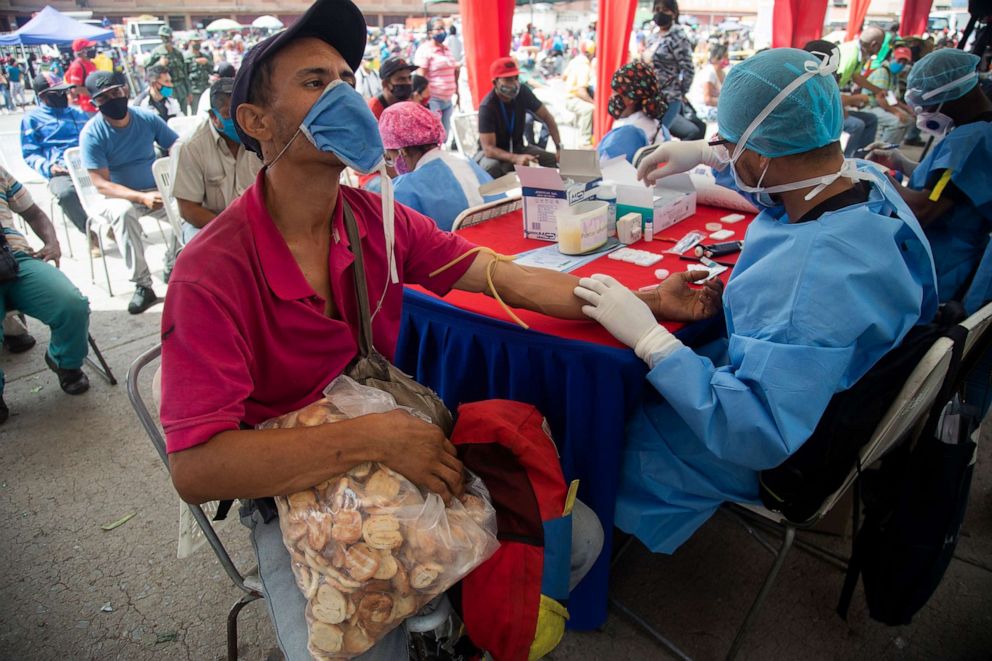 PHOTO: A health worker takes a blood sample for a quick COVID-19 test from man who works selling cookies at the Coche food market in Caracas, Venezuela, June 23, 2020.