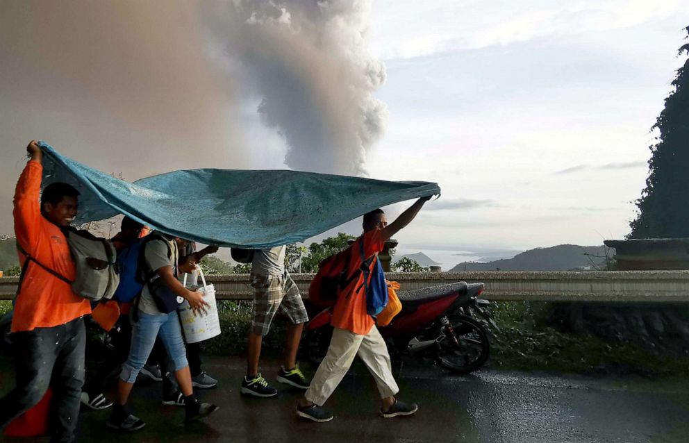 PHOTO: People take cover under a large plastic sheet as a column of ash spews from erupting Taal Volcano over Tagaytay city, Philippines, Jan. 12, 2020. 