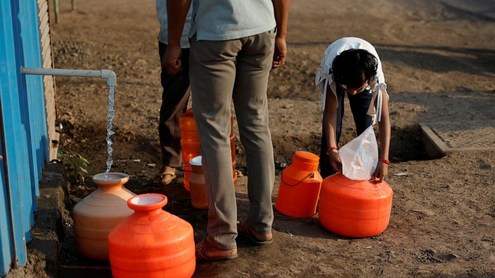 PHOTO: A girl covers a pot filled with water with a plastic sheet to protect it from dust next to a water ATM machine in Solapur, India, March 3, 2025.
