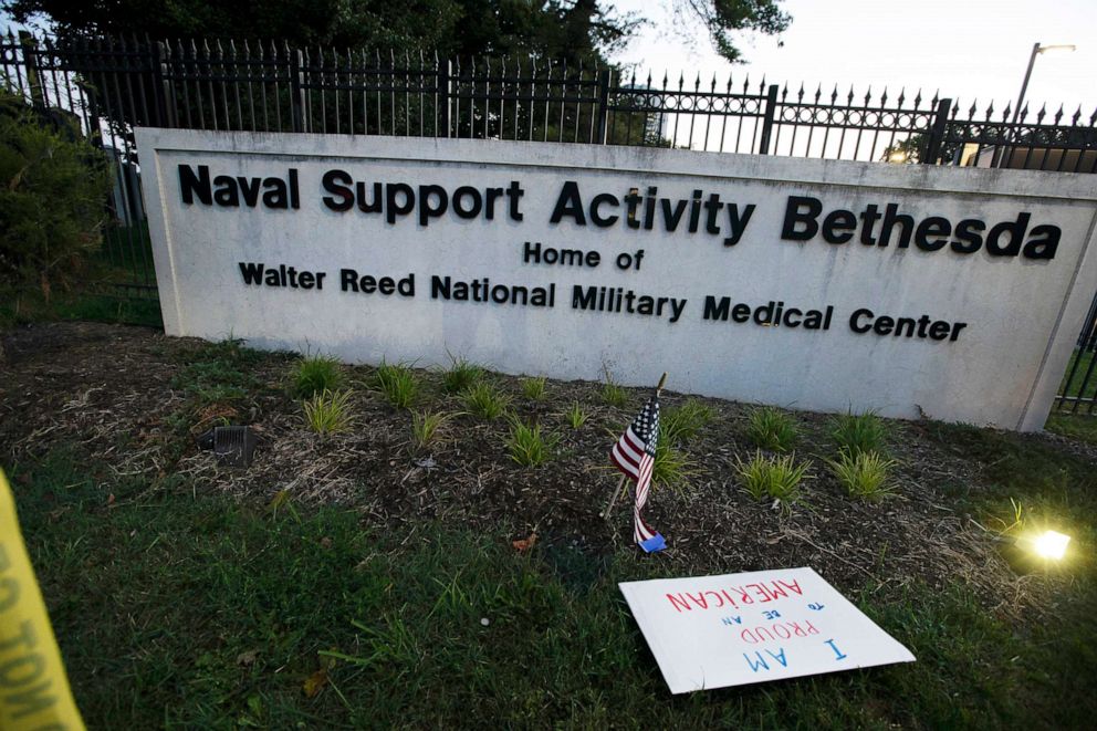 PHOTO: A sign that reads " I am proud to be American" and a flag are left at the main gate of Walter Reed National Military Medical Center in Bethesda, Md., Oct. 3, 2020. Stricken by COVID-19, Trump was flown to Walter Reed on Oct. 2.