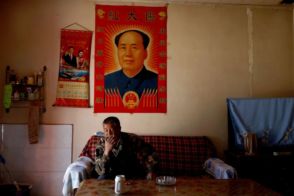 PHOTO: Wang Yinji sits in front of posters while smoking at his house in a village near the edge of the Gobi desert on the outskirts of Wuwei, China, April 14, 2021.