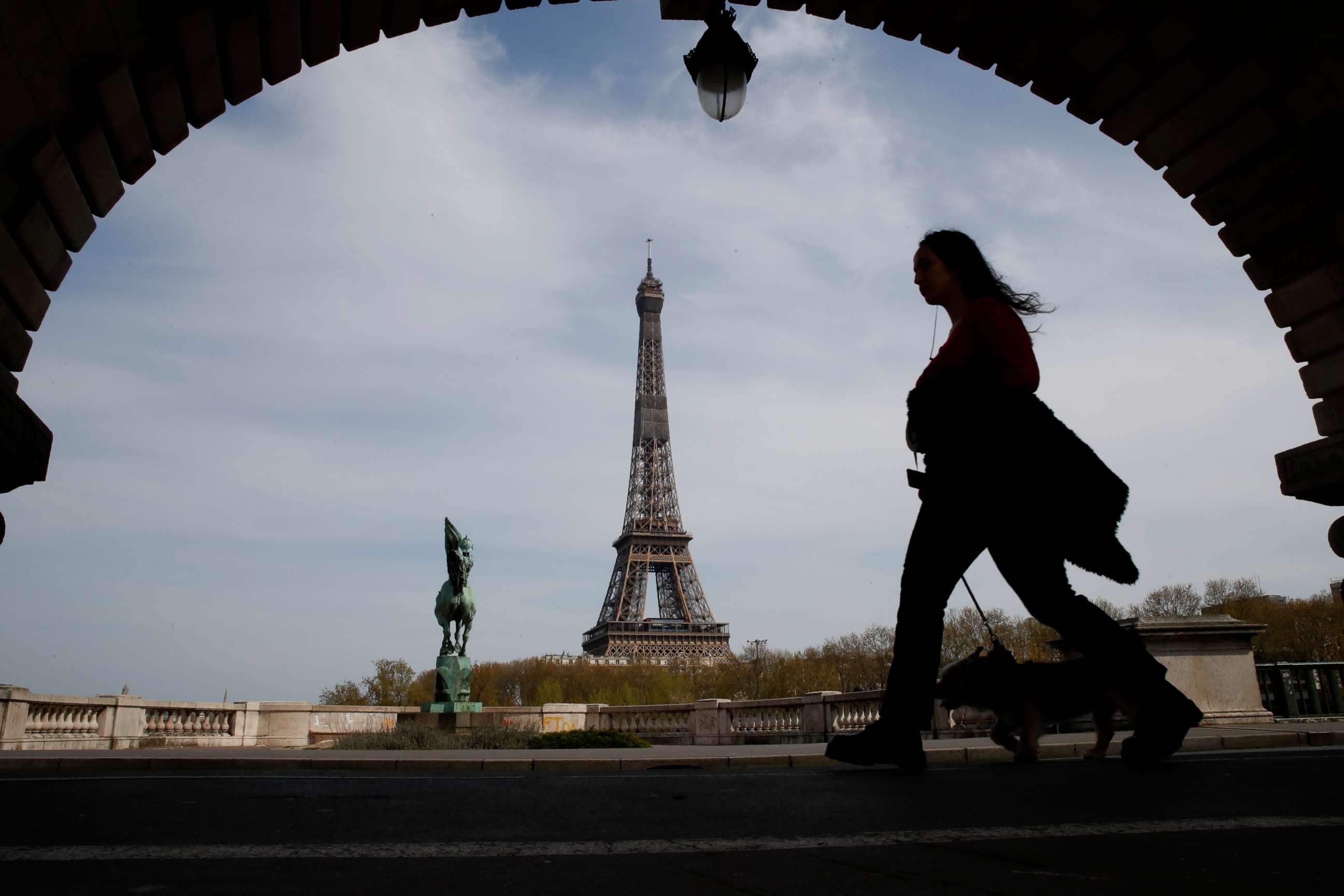 PHOTO: A woman walks her dog on a bridge with the Eiffel tower in the background in Paris, France, on April 7, 2020, during a nationwide confinement to counter the novel coronavirus.