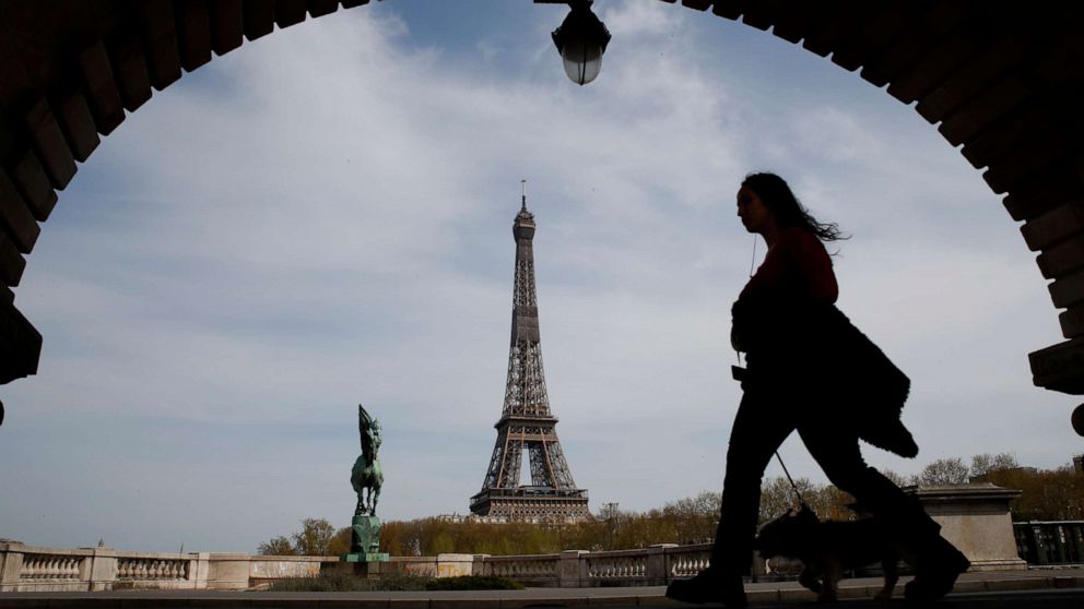 PHOTO: A woman walks her dog on a bridge with the Eiffel tower in the background in Paris, France, on April 7, 2020, during a nationwide confinement to counter the novel coronavirus.