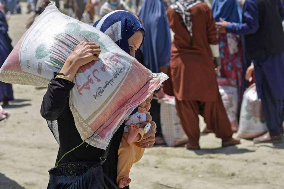 PHOTO: A woman carries her child and a sack of rice distributed to people in need by the Afghan Ministry of Refugees in cooperation with China, in Kabul on June 8, 2022.