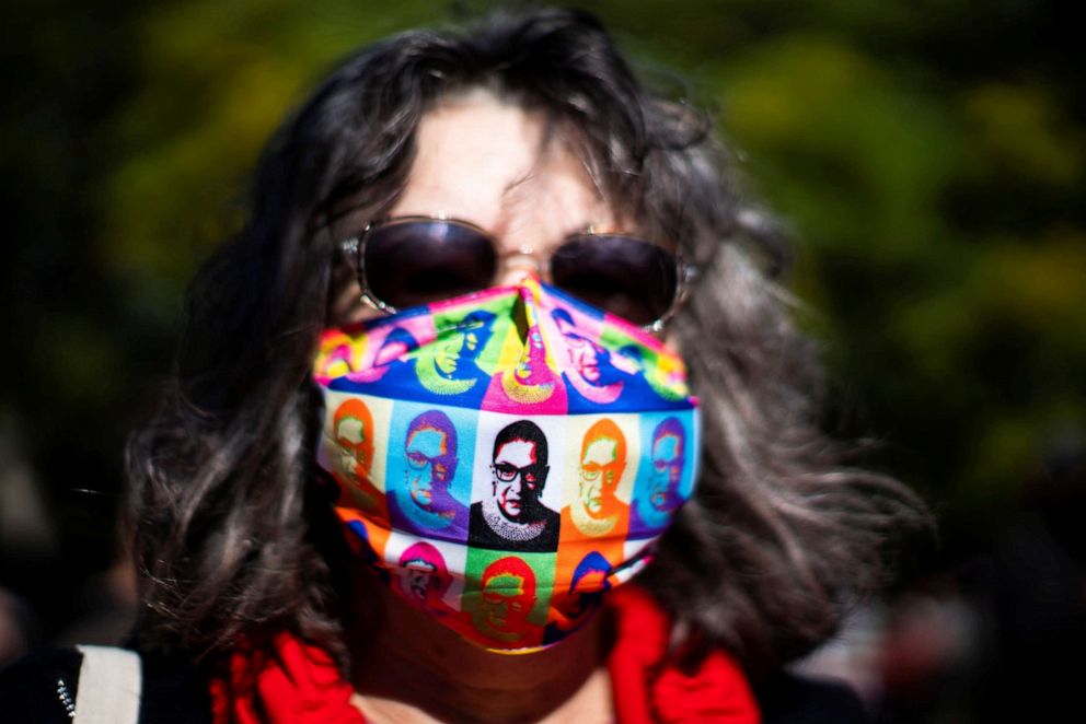 PHOTO: A woman wears a face mask with images of late Justice Ruth Bader Ginsburg as people take part in the 2020 Women's March at Washington Square park in New York City, Oct. 17, 2020.
