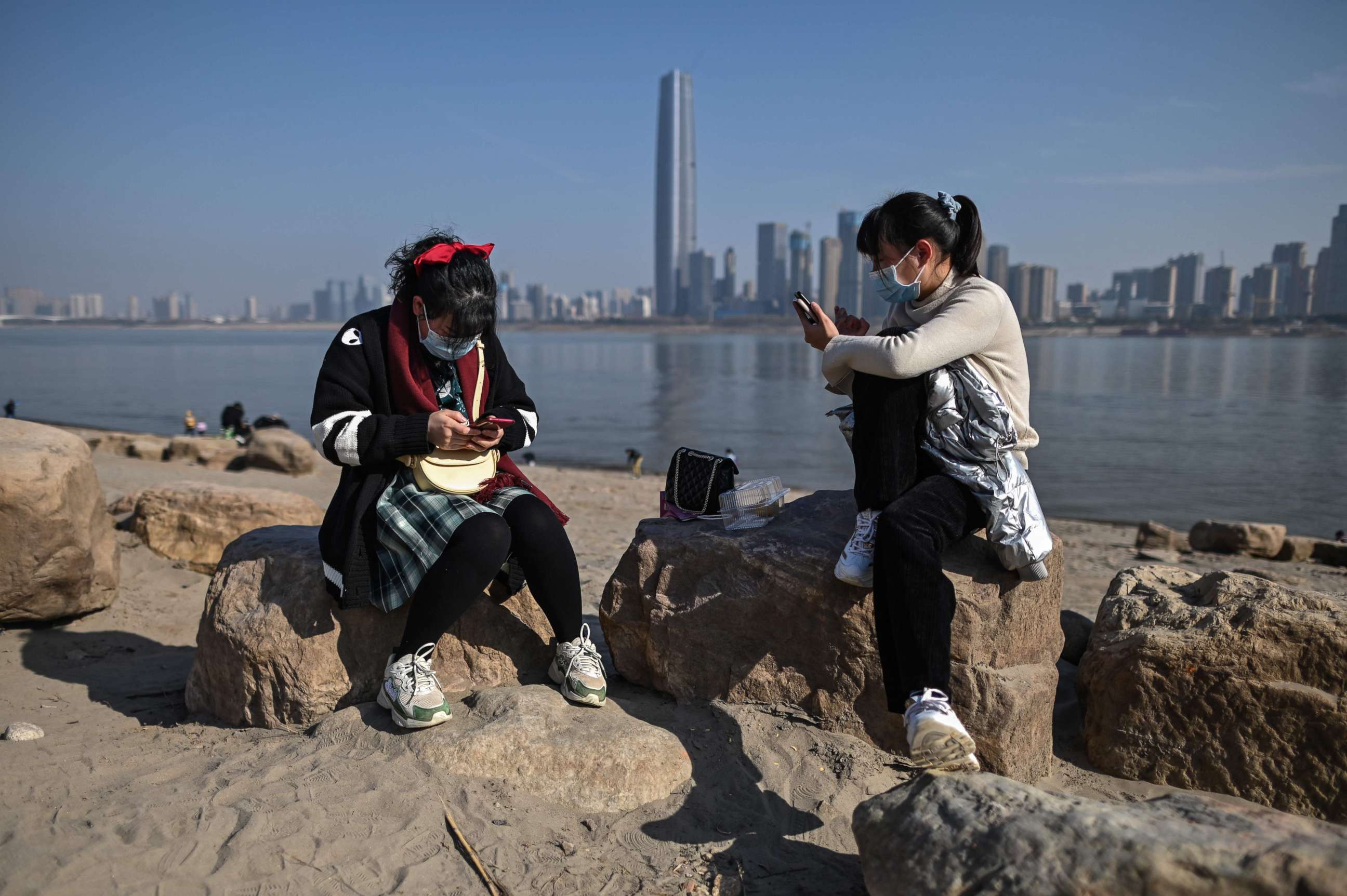 PHOTO: Women wearing face masks look at their mobile phones on the banks of the Yangtze River in Wuhan, China's central Hubei province on January 19, 2021. 