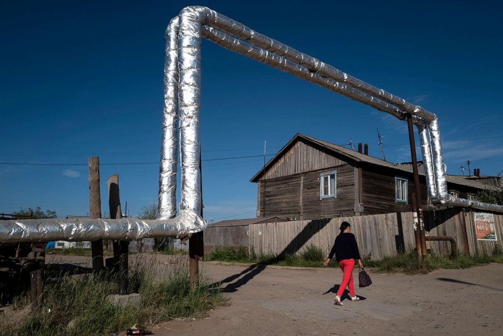 PHOTO: A woman walks under a pipe built above ground due to the permafrost that the city is built upon in Yakutsk, Russia on July 2, 2019. Melting permafrost is altering Siberia's landscape and the region's economy.
