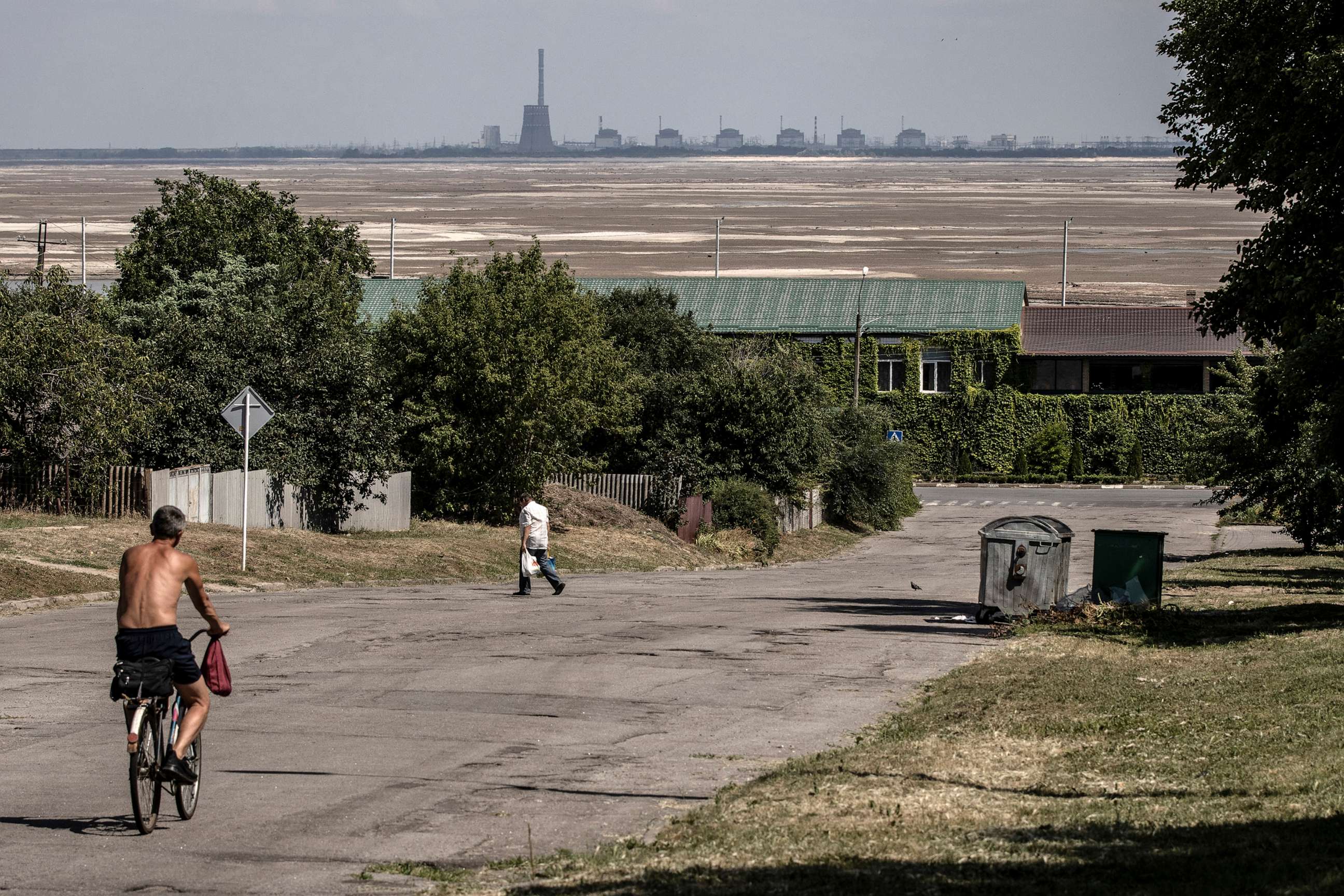 PHOTO: Residents pass along a street in Nikopol, with the Zaporizhzhia Nuclear Power Plant in the background, behind an expanse of sand exposed after the destruction of the Nova Kakhovka Dam, in Ukraine, on July 3, 2023.