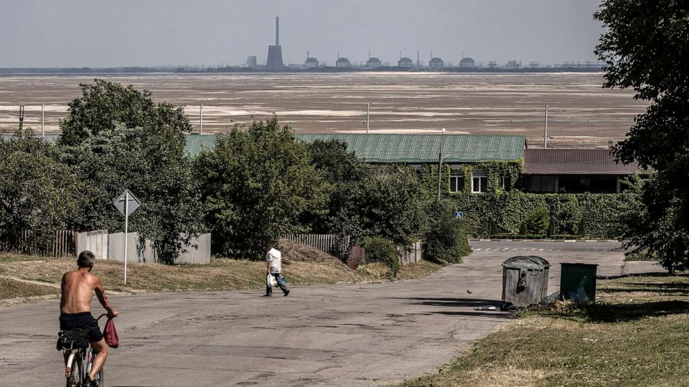 PHOTO: Residents pass along a street in Nikopol, with the Zaporizhzhia Nuclear Power Plant in the background, behind an expanse of sand exposed after the destruction of the Nova Kakhovka Dam, in Ukraine, on July 3, 2023.