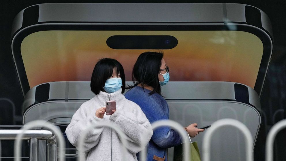 PHOTO: A woman wearing face masks waits for their bus at a bus stop displaying an iPhone ad in Beijing on Oct. 30, 2022. Access to an industrial zone in the central Chinese city of Zhengzhou was suspended in early November.