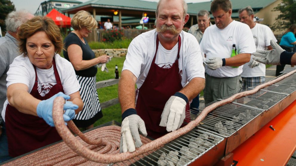 In this Sept. 9, 2014 photo, Mabel and Larry Schubert help lay out a 100 foot-long bratwurst on a grill at the Silver Creek Saloon in Belleville, Ill. 