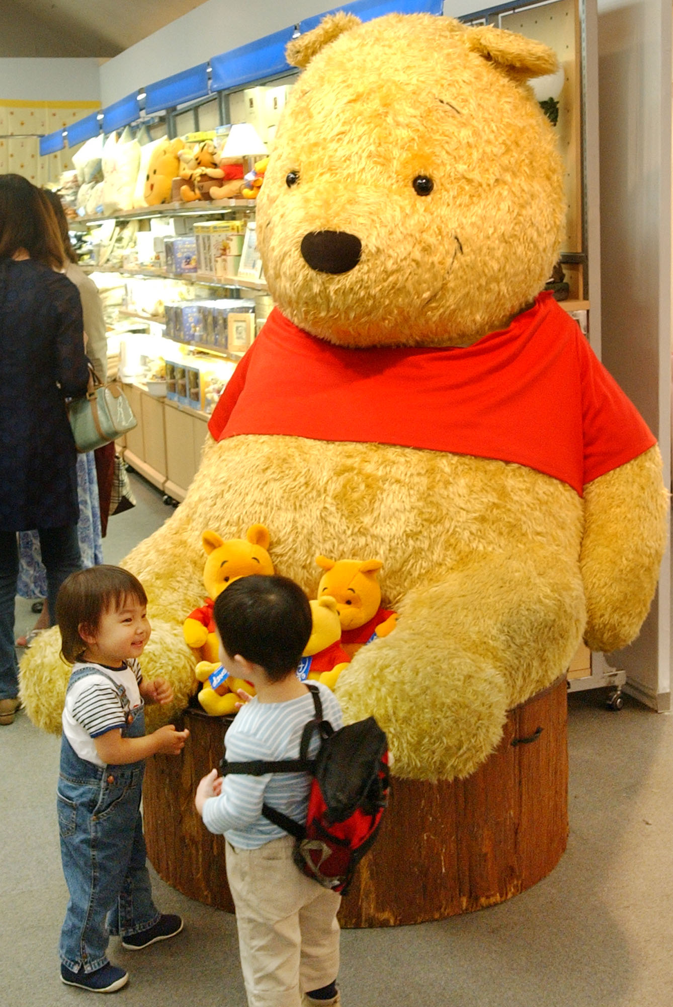 Two boys chat in front of a giant stuffed doll of Winnie-The-Pooh at the "World of Winnie-The-Pooh" exhibition at a Tokyo department store in this April 24, 2002 photo.