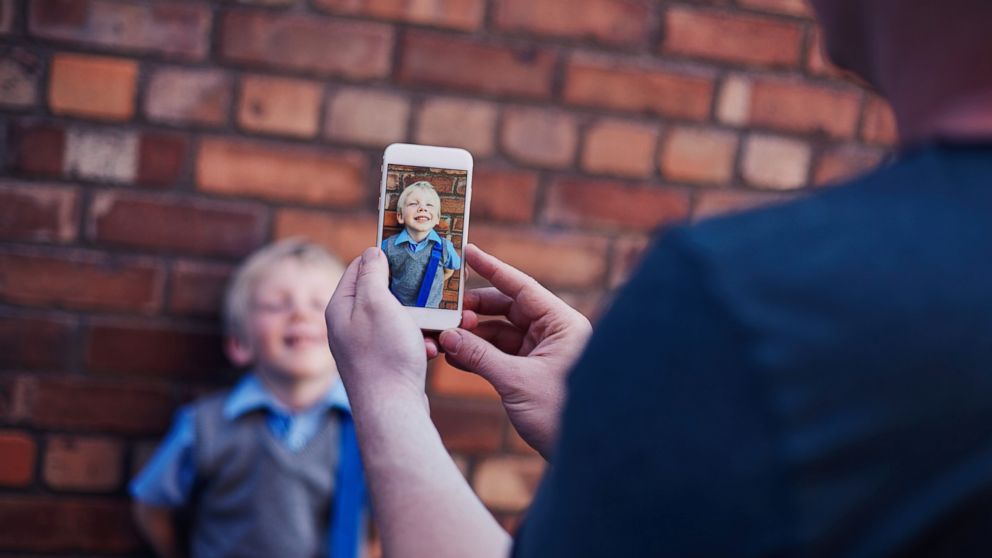 Father using a smart phone to take a photo of his son on his first day school.