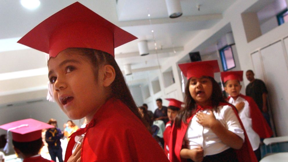 Silvia Torres, left, places her hand over her heart as she does the Pledge of Allegiance with his fellow classmates at the beginning of their kindergarten graduation at Cahuenga Elementary School in Los Angeles. 