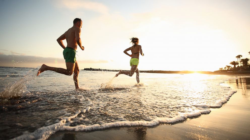 A man and woman run on beach at sunset.