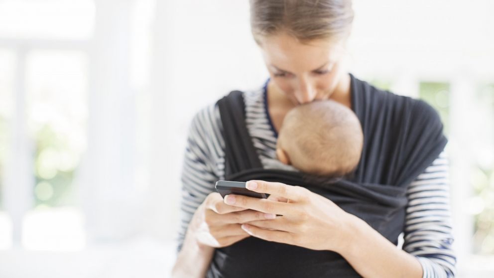 A mother sends a text message while holding her baby in this stock image.