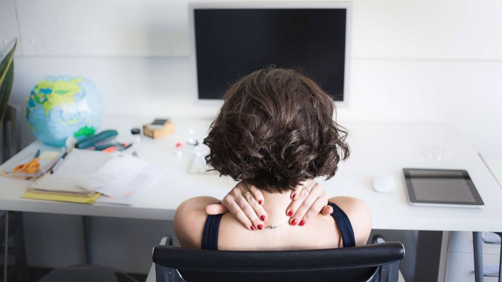 PHOTO: A young woman massages her neck at a desk in an undated stock photo.