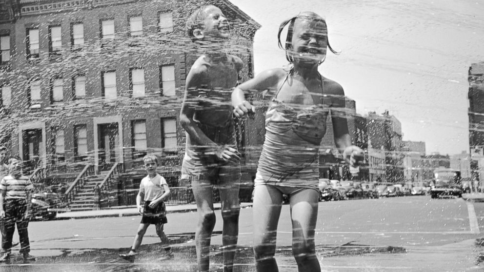 Two children jump through a fire hydrant's spray on a street in New York, circa 1950.