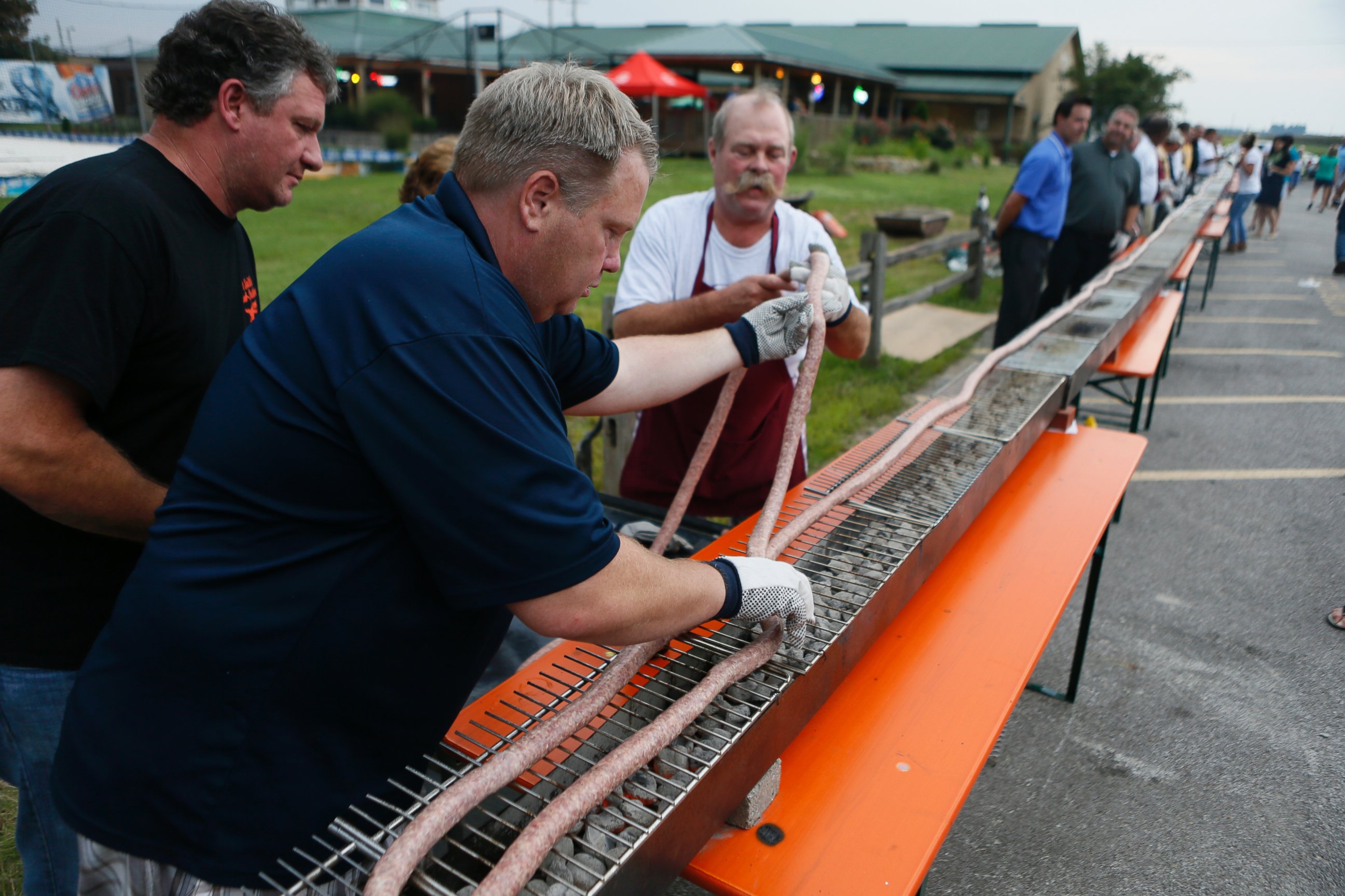 PHOTO: From left: Jeff Butzinger looks on as James Sinovic helps Larry Schubert lay out the 100 foot long bratwurst on the grill at the Siver Creek Saloon in Belleville. 