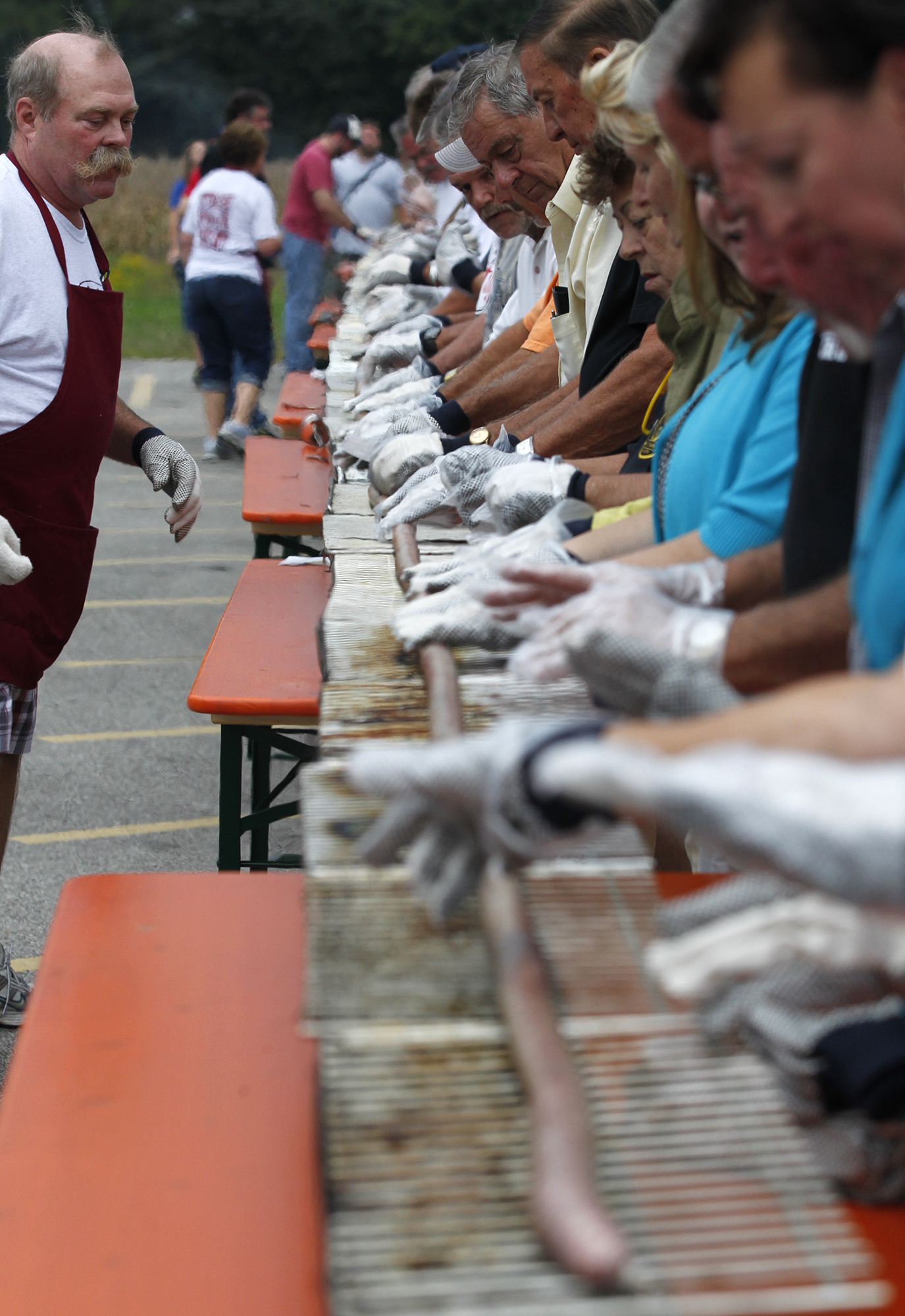 PHOTO: Larry Schubert looks on as volunteers roll the bratwurst on the grill. 