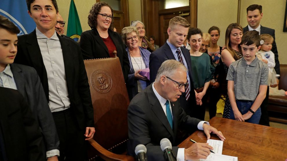 Katrina Spade, upper left, the founder and CEO of Recompose, a company that hopes to use composting as an alternative to burying or cremating human remains, looks on Tuesday, May 21, 2019, as Washington Gov. Jay Inslee, center, signs a bill into law 