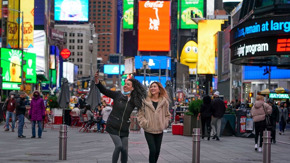 Pedestrians pose for pictures in Times Square, Monday, Nov. 15, 2021, in New York. Even as visitors again crowd below the jumbo screens in New York’s Times Square, the souvenir shops, restaurants, hotels and entrepreneurs within the iconic U.S. landm