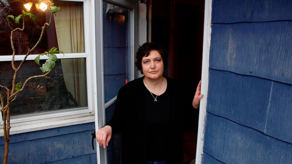 In this April 29, 2020 photo, Julie Hitchcock stands in her back doorway in Milwaukee. Hitchcock, 49, said she worries about getting sick or unknowingly infecting someone else, anxiety that's heightened because she was on a ventilator for two weeks l