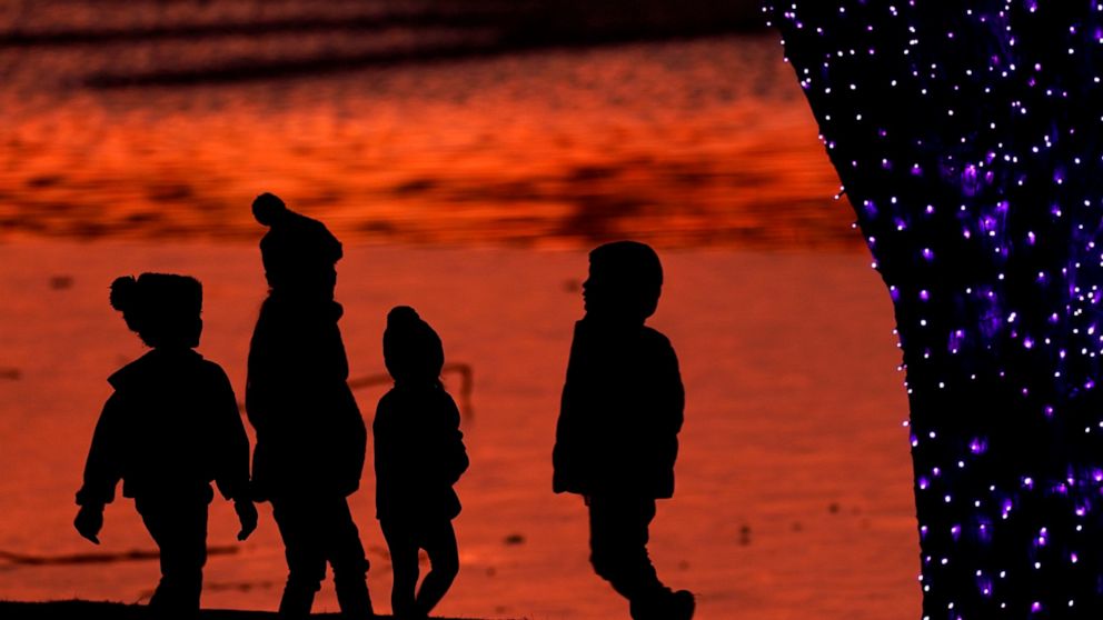 FILE - In this Saturday, Dec. 26, 2020 file photo, children are silhouetted against a pond as they look at Christmas lights at a park in Lenexa, Kan. Balancing checkbooks and paying in cash are out, credit cards and digital wallets are in. When today