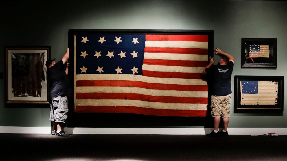 In this Wednesday, June 12, 2019 photo, workmen hang a Federal Era flag as part of the new exhibit "A New Constellation: A Collection of Historic 13-Star Flags," at the Museum of the American Revolution in Philadelphia. The exhibit featuring 40 rare,
