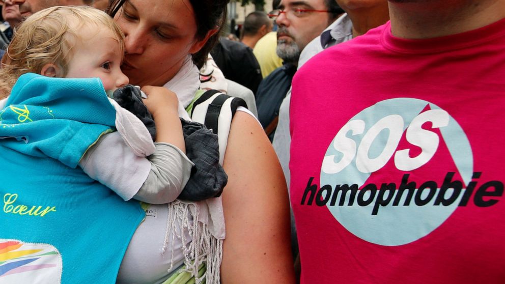 FILE - In this Saturday, June 28, 2014 file photo a woman kisses a baby next to a man wearing a shirt reading "SOS Homophobia" during the annual Gay Pride march in Paris, France. Single women and lesbians in France won't have to go abroad to have bab