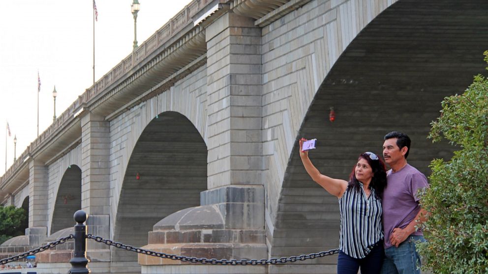 Claudia and Rafael Lopez take a selfie in front of the London Bridge in Lake Havasu City, Ariz., on Saturday, Sept. 25, 2021. Lake Havasu City is playing up its roots with a month of celebratory events marking the 50th anniversary of the dedication o