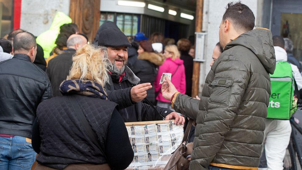A man buys a Christmas lottery ticket from a street seller in Madrid, Spain, Saturday, Dec. 21, 2019. Spain's bumper Christmas lottery draw known as El Gordo, or The Fat One, will be held on Dec. 22. (AP Photo/Paul White)