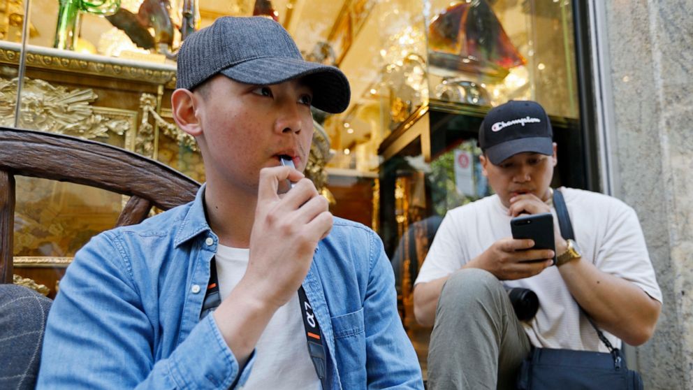 In this Monday, June 17, 2019, photo, Joshua Ni, 24, and Fritz Ramirez, 23, vape from electronic cigarettes in San Francisco. San Francisco supervisors are considering whether to move the city toward becoming the first in the United States to ban all