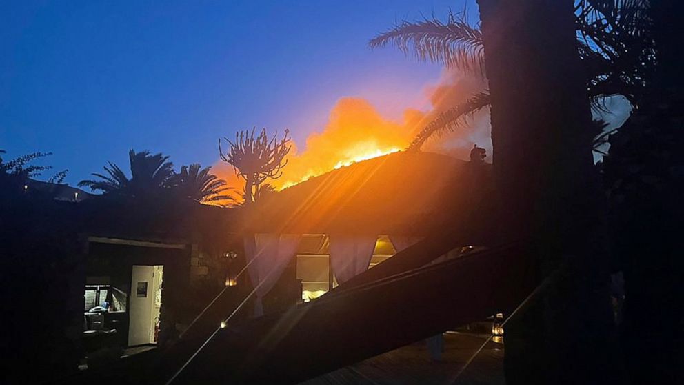 Flames burn beyond fashion designer Giorgio Armani's villa on the Sicilian island of Pantelleria, Wednesday, Aug. 17, 2022. The designer and his guests evacuated overnight to a boat in the port, and the flames stopped short of the property, according