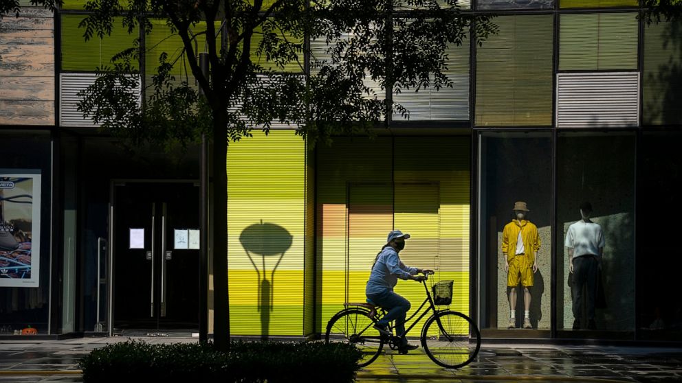 FILE - A woman wearing a face mask rides a bicycle past stores closed for COVID-19 control at a shopping mall in Beijing, Tuesday, May 17, 2022. Neither inflation nor the war in Ukraine are threatening to take a bite out of the luxury fashion market,