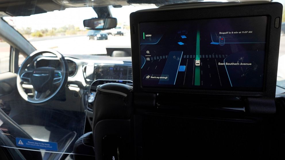 A Waymo minivan moves along a city street as an empty driver's seat and a moving steering wheel drive passengers during an autonomous vehicle ride, as passengers view a detailed viewing screen, Wednesday, April 7, 2021, in Chandler, Ariz. Waymo, a un