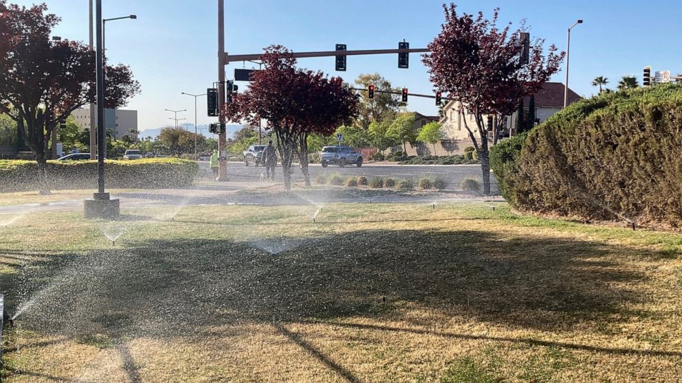 Sprinklers water grass near a street corner Friday, April 9, 2021, in the Summerlin neighborhood of northwest Las Vegas. A desert city built on a reputation for excess wants to become a model for restraint with a first-in-the-nation policy limiting w
