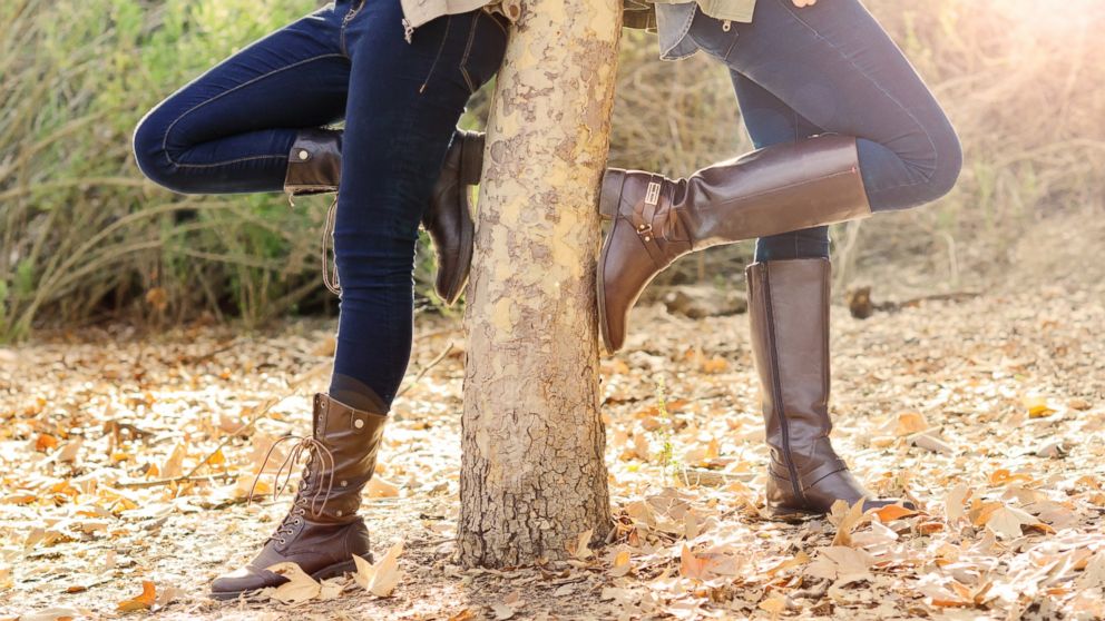 Two women wearing boots stand in autumn leaves.