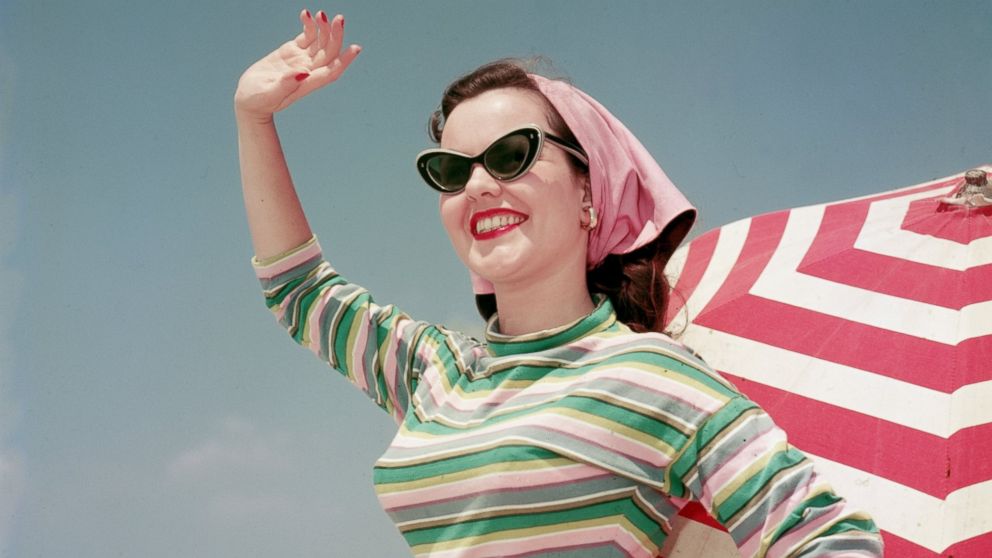 Vintage sunglasses are making a comeback for the summer season. Seen here, a model waves on the beach, circa 1956.